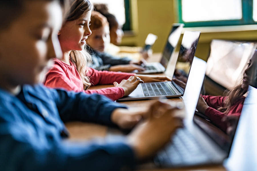  Middle school age students work at laptops at a desk 