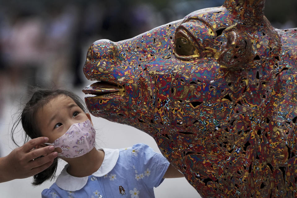 A child wearing a face mask takes a closer look at a bull sculpture titled "Five Bulls Gathering Fortune" at the Wangfujing shopping district in Beijing, Tuesday, Aug. 9, 2022. (AP Photo/Andy Wong)