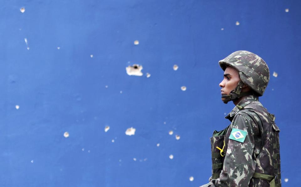 A Brazilian Army soldier walks past bullet holes in a wall during an operation in the Mare slums complex in Rio de Janeiro March 26, 2014. Brazil will deploy federal troops to Rio de Janeiro to help quell a surge in violent crime following attacks by drug traffickers on police posts in three slums on the north side of the city, government officials said on Friday. Less than three months before Rio welcomes tens of thousands of foreign soccer fans for the World Cup, the attacks cast new doubts on government efforts to expel gangs from slums using a strong police presence. The city will host the Olympics in 2016. REUTERS/Ricardo Moraes (BRAZIL - Tags: CRIME LAW)