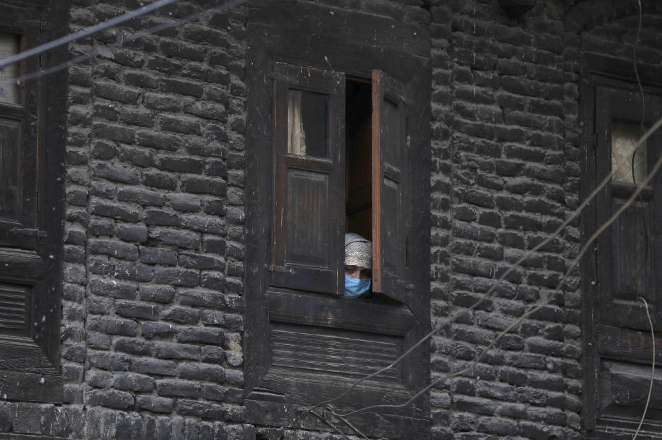 FILE- In this April 6, 2020 file photo, a Kashmiri woman wearing protective mask watches through a window of her house as an Indian policeman makes markings for people to maintain social distance at a market in Srinagar, Indian controlled Kashmir. India, a bustling country of 1.3 billion people, has slowed to an uncharacteristic crawl, transforming ordinary scenes of daily life into a surreal landscape. The country is now under what has been described as the world’s biggest lockdown, aimed at keeping the coronavirus from spreading and overwhelming the country’s enfeebled health care system. (AP Photo/Mukhtar Khan, File)