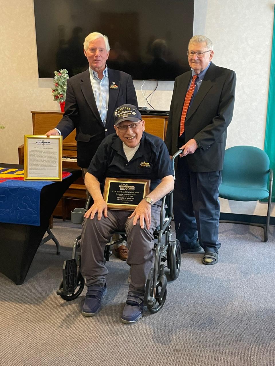 Retired U.S. Navy Chief Petty Officer Ed August Sr. accepts a citation and plaque commemorating the naming of two “cruiser compartments” aboard the USS Salem museum ship after him. Joining him at Linn Health & Rehabilitation on Dec. 6 are U.S. Navy Cruiser Sailors Association President David Blomstrom, right, and Secretary James Chryst.