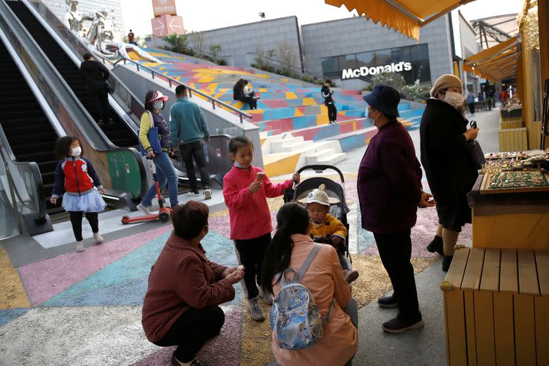 Children enjoy ice creams as a woman wearing a face mask tries on earrings near an outdoor market inside a shopping complex in Beijing