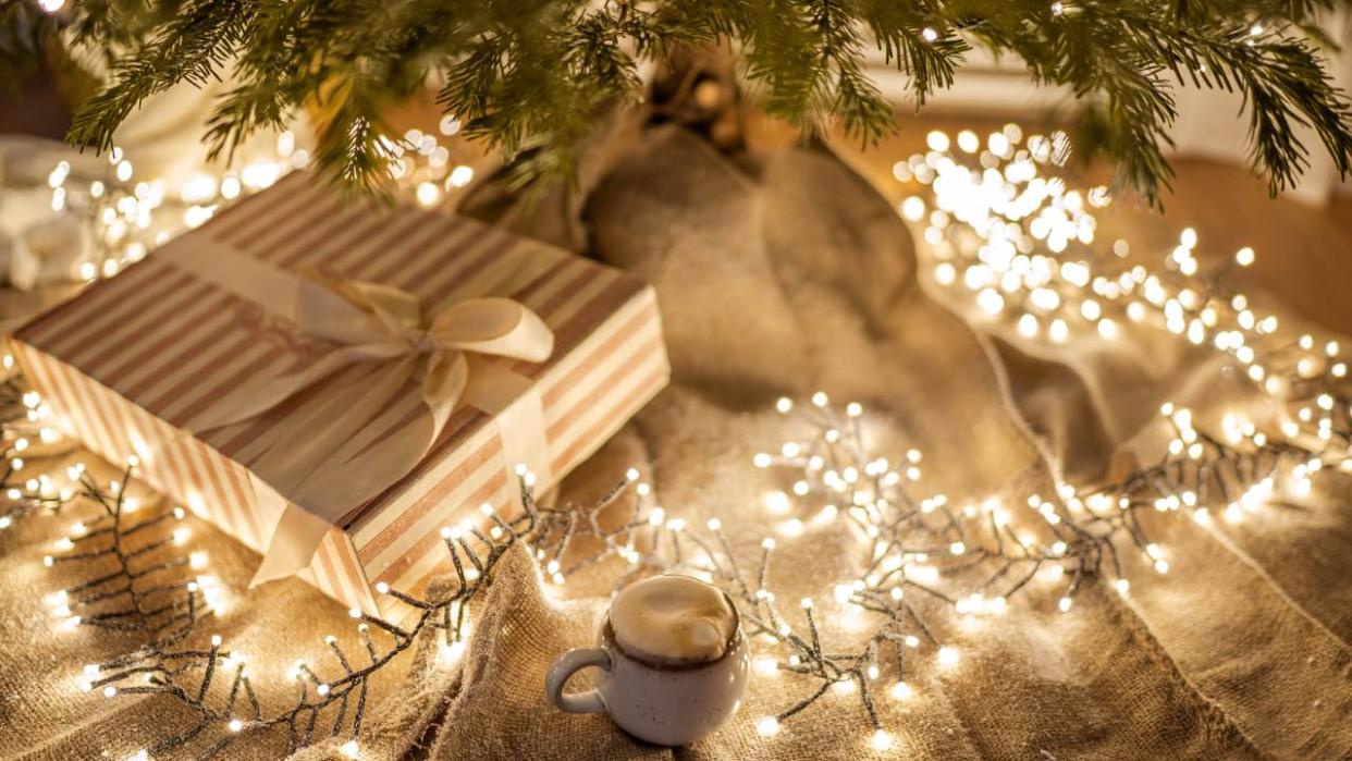  A string of yellow Christmas lights wrapped around presents under the Christmas tree. 