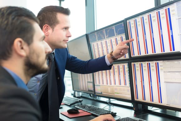 Two businesmen looking at financial information on an array of computer screens.