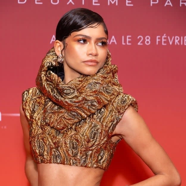 Zendaya in an ornate gold-patterned outfit with high collar, posing on the red carpet