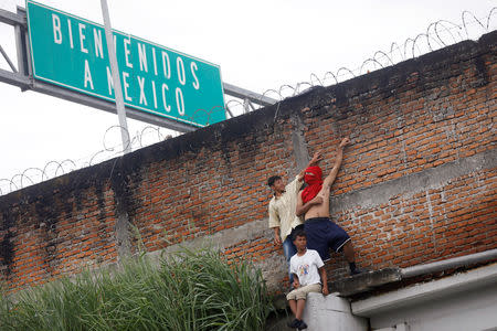 Honduran migrants, part of a caravan trying to reach the U.S., are pictured behind a wall as they avoid the border checkpoint in Ciudad Hidalgo, Mexico, October 19, 2018. REUTERS/Edgard Garrido