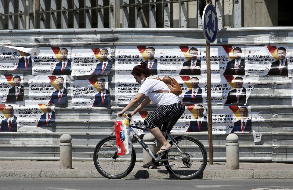 A woman rides a bicycle past electoral campaign posters of the largest opposition party VMRO-DPMNE set on a construction fence along a street in Skopje, North Macedonia on Saturday, July 11, 2020. North Macedonia holds its first parliamentary election under its new country name this week, with voters heading to the polls during an alarming spike of coronavirus cases in the small Balkan nation. (AP Photo/Boris Grdanoski)