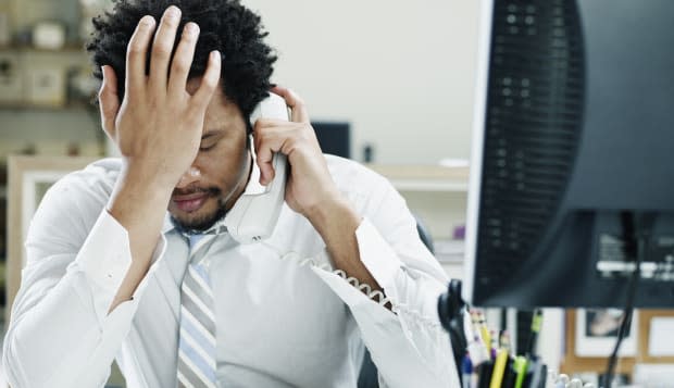 Businessman on phone at desk hand on forehead