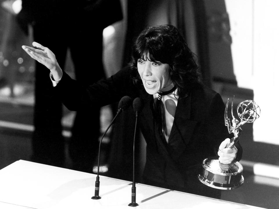 Black and white photo of Lily being animated and speaking at a podium while holding her Emmy trophy.