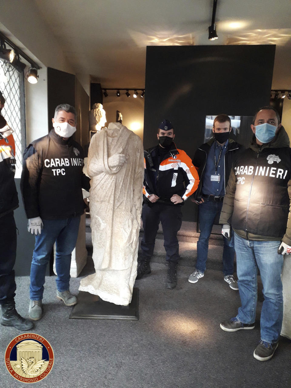 Carabinieri (Italian paramilitary police) officers of the art squad’s archaeological unit pose with a headless Roman statue wearing a draped toga in Brussels on Wednesday, Feb. 3, 2021. Italian police say they have recovered a 1st century Roman statue that was stolen from an archaeological site in 2011 and found in a Belgian antiques shop by two off-duty Italian art squad police officers. The Carabinieri art squad said Monday that an Italian businessman who used a Spanish pseudonym has been referred to prosecutors for further investigation into allegations he received and then exported the statue abroad. The statue has been valued at 100,000 euro. (Carabinieri via AP)