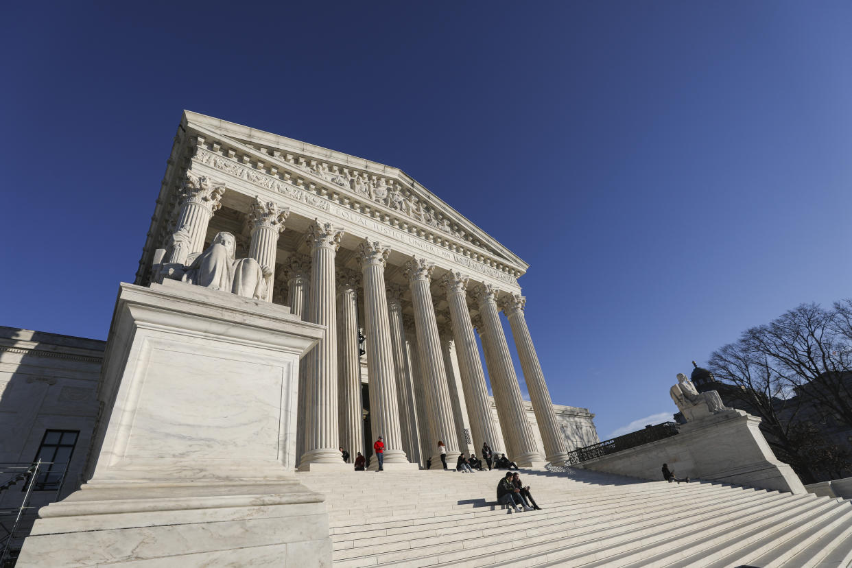 Two people sit on the steps of the Supreme Court, with other tourists at the top under its colonnades.