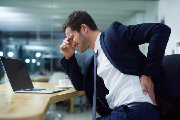 Si trabajas sentado trata de no curvar ni tensionar la espalda. Mantenerla en posición vertical, bien apoyada en el respaldo del asiento y descansar los pies sobre un reposapiés te aliviará.(Foto: Getty)