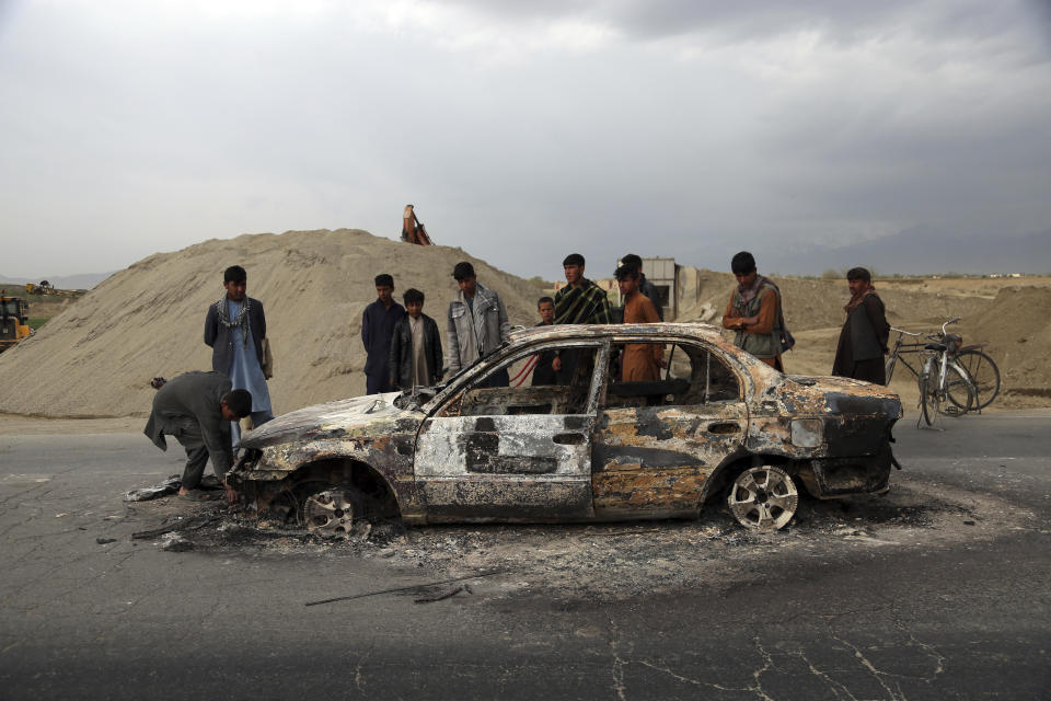 FILE - In this April 9, 2019, file photo, Afghans watch a civilian vehicle burnt after being shot by U.S. forces following an attack near the Bagram Air Base, north of Kabul, Afghanistan. Afghanistan has been at war for more than 40 years, first against the invading Soviet army that killed more than 1 million people, then feuding mujahedin groups in a bitter civil war followed by the repressive Taliban rule and finally the latest war that began after the 2001 U.S.-led coalition invasion that toppled the Taliban government. (AP Photo/Rahmat Gul, File)