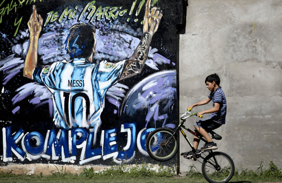 En la fotografía del 5 de diciembre de 2019, a un chico pasea en su bicicleta frente a un mural con la imagen del astro argentino Lionel Messi en La Bajada, Rosario, Argentina. Cuando Messi era pequeño, el fútbol compartía su atención con paseos en bicicleta junto a amigos, levantar chozas con ramas y piedras en un baldío, jugar a la escondidas o robar limones de la planta de un vecino para beber limonada en las tardes de verano durante su niñez en el modesto barrio La Bajada, en el sur su ciudad natal. (AP Foto/Natacha Pisarenko)