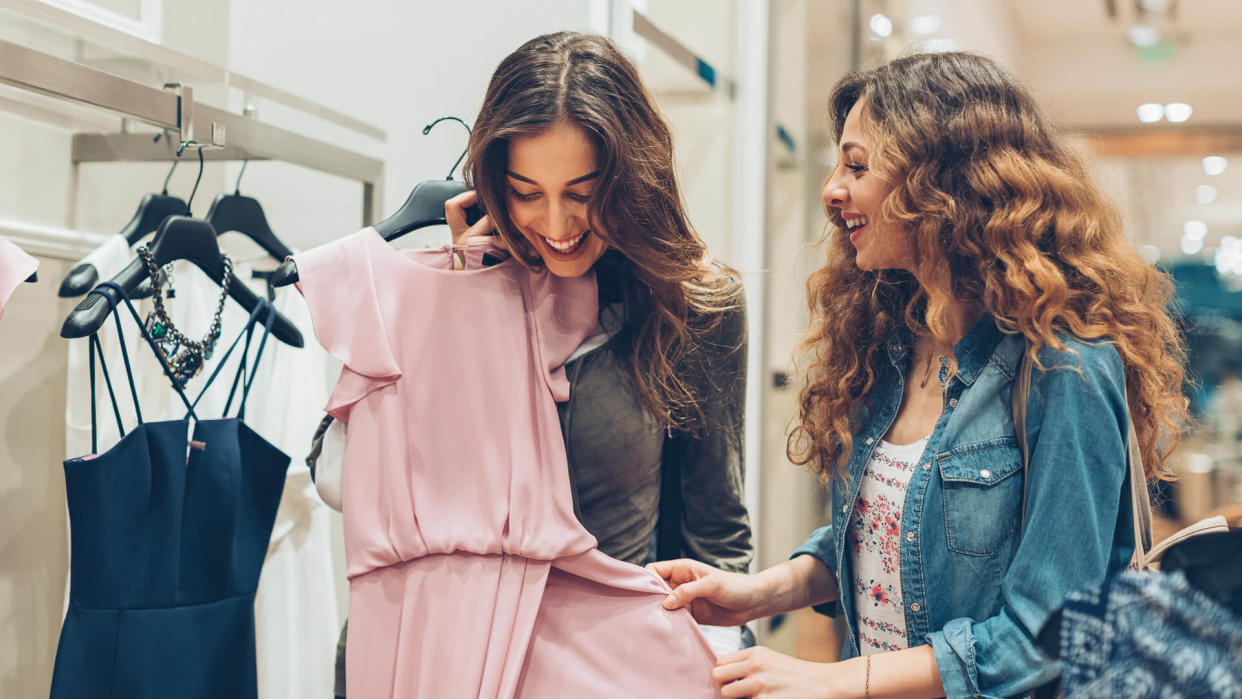 Two young women choosing dresses in a luxury fashion store.