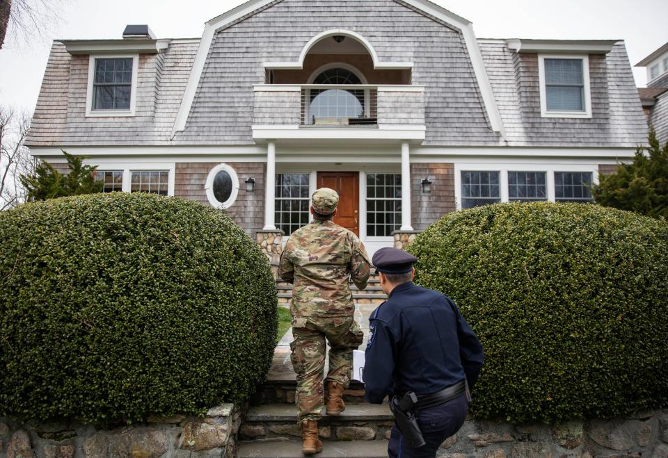 Rhode Island Air National Guard Tsgt. William Randall, left, and Westerly police officer Howard Mills approach a home while looking for New York license plates in driveways to inform them of self quarantine orders, Saturday, March 28, 2020, in Westerly, R.I.