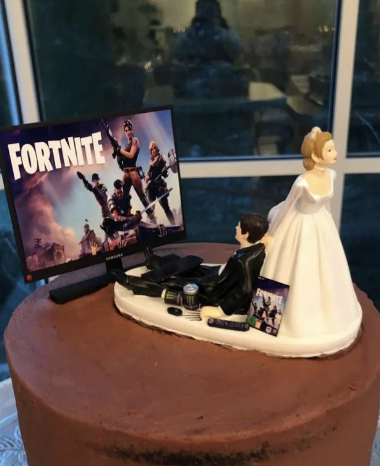 A wedding cake topper of a bride pulling her groom from a game of "Fortnite"