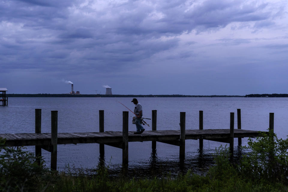 A fisherman walks along a dock on the St. Johns River as a coal-fired power plant stands in the background, in Palatka, Fla., Wednesday, April 14, 2021. After months in a prison cell, Warren Williams longed to fish the St. Johns again. He looked forward to spending days outdoors in his landscaping job, and to writing poems and music in his free time. (AP Photo/David Goldman)
