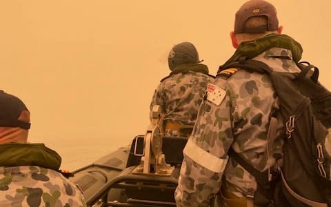 A tender from HMAS Choules motors through smoke haze off the coast of Mallacoota - Credit: AP