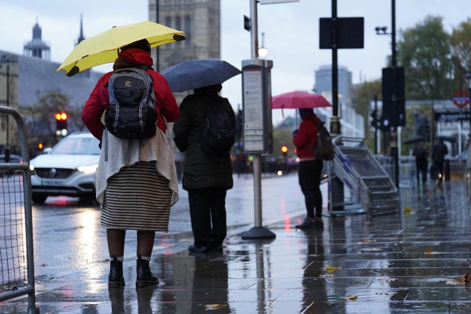 People hold umbrellas as they wait in the rain at a bus stop in Whitehall, London (PA)