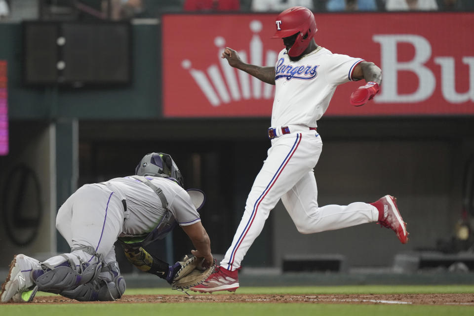 Texas Rangers' Adolis Garcia, right, beats a tag by Colorado Rockies catcher Elias Diaz at home plate to score on a sacrifice fly by Rangers' Robbie Grossman during the first inning of a baseball game in Arlington, Texas, Saturday, May 20, 2023. (AP Photo/LM Otero)