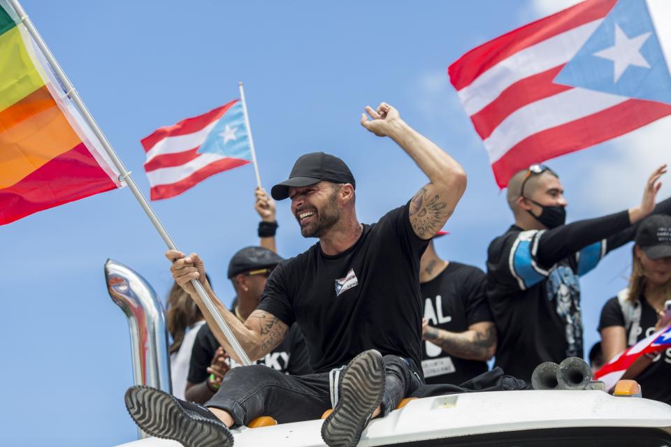 En esta foto del 22 de julio de 2019, Ricky Martin, con una bandera de orgullo gay, participa en una manifestación en San Juan para exigir la renuncia del gobernador de Puerto Rico Ricardo Rosselló. (AP Foto/Dennis M. Rivera Pichardo)