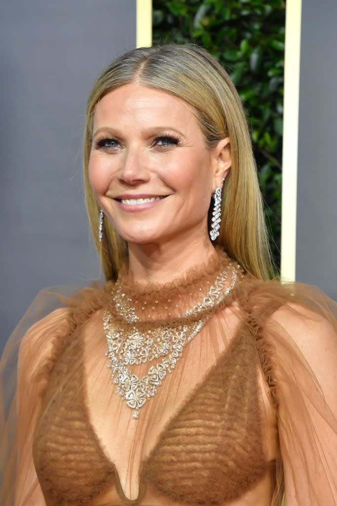 Gwyneth Paltrow smiling in an elegant dress with intricate necklace and dangling earrings