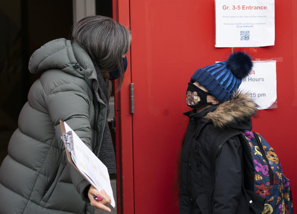A school administrator, left, asks a student if his parents have completed a form granting permission for random COVID-19 testing as he arrives at P.S. 134 Henrietta Szold Elementary School, Monday, Dec. 7, 2020, in New York. Public schools reopened for in-school learning Monday after being closed since mid-November. (AP Photo/Mark Lennihan)