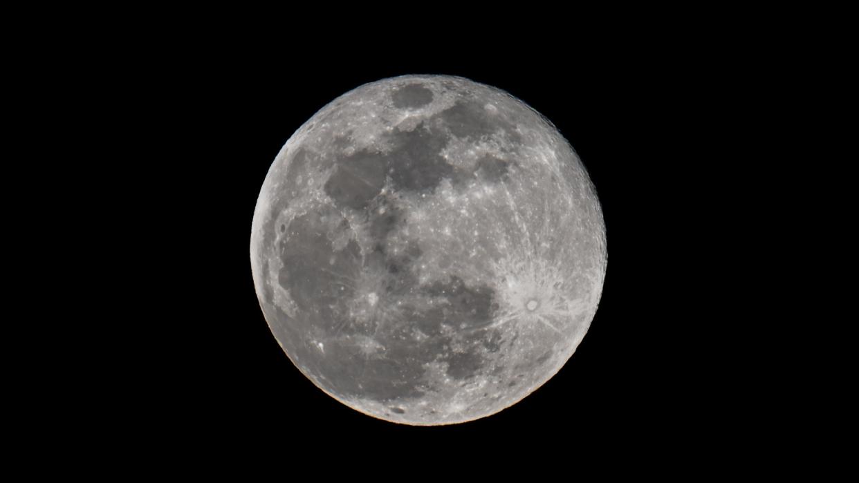  A bright full moon stands out starkly against a perfectly black night sky. 