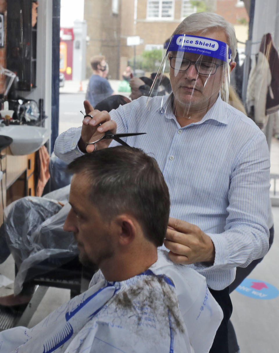 A barber cuts hair at Northfields Barber as it opens for the first time after the COVID-19 lockdown in London, Saturday, July 4, 2020. England is embarking on perhaps its biggest lockdown easing yet as pubs and restaurants have the right to reopen for the first time in more than three months. In addition to the reopening of much of the hospitality sector, couples can tie the knot once again, while many of those who have had enough of their lockdown hair can finally get a trim. (AP Photo/Frank Augstein)