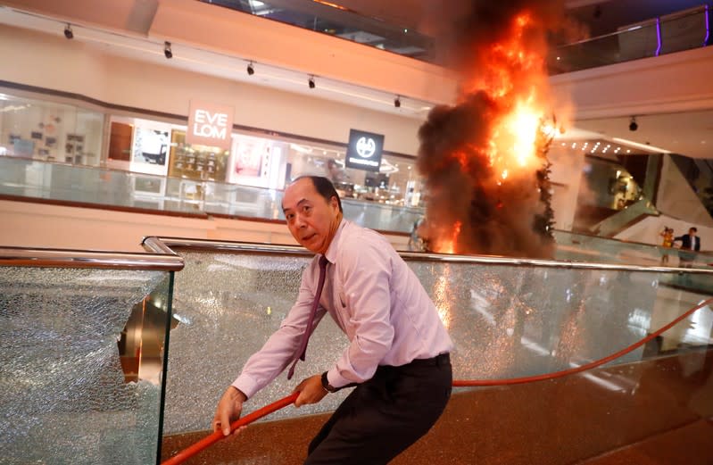 A man reacts as he tries to extinguish a burning Christmas tree at Festival Walk mall in Kowloon Tong, Hong Kong