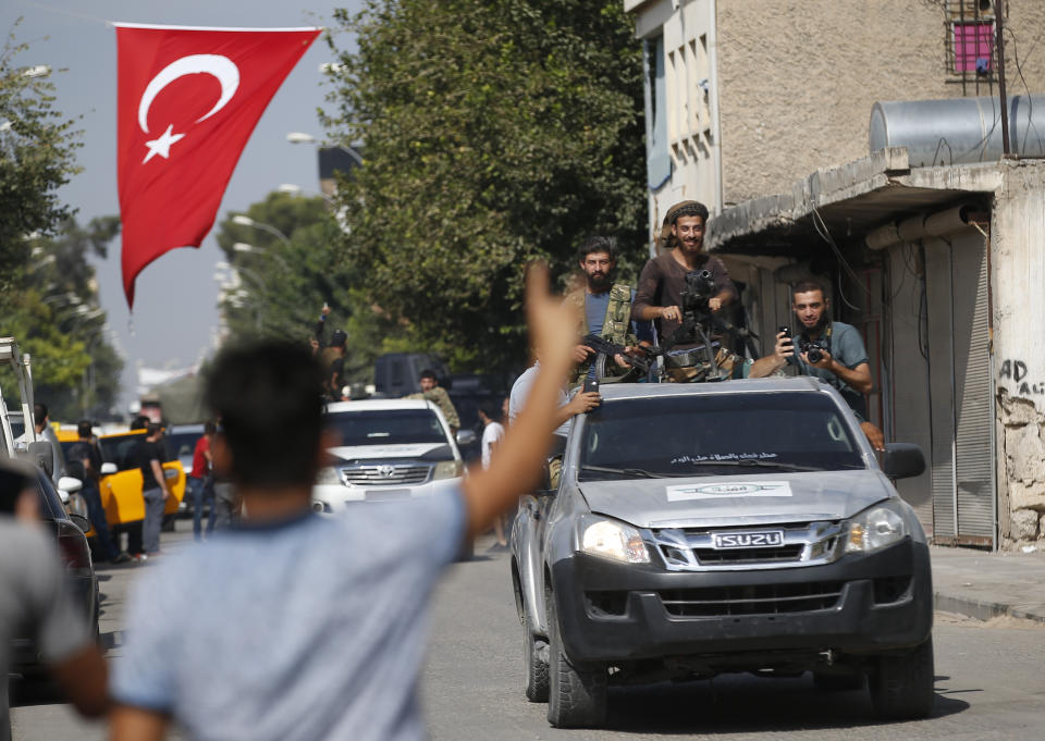 Local residents cheer as Turkish-backed Syrian opposition fighters drive around the border town of Akcakale, Sanliurfa province, southeastern Turkey, on their way to Tal Abyad, Syria, Monday, Oct. 14, 2019. Syrian troops entered Monday several northern towns and villages getting close to the Turkish border as Turkey's army and opposition forces backed by Ankara marched south in the same direction raising concerns of a clash between the two sides as Turkey's invasion of northern Syria entered its sixth day. (AP Photo/Lefteris Pitarakis)