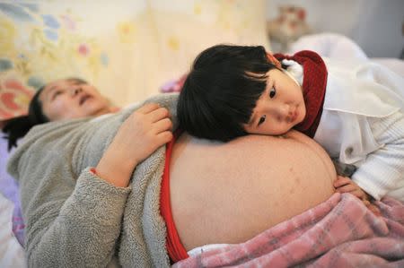 Li Yan (L), pregnant with her second child, lies on a bed as her daughter places her head on her mother's stomach in Hefei, Anhui province February 20, 2014. REUTERS/China Daily