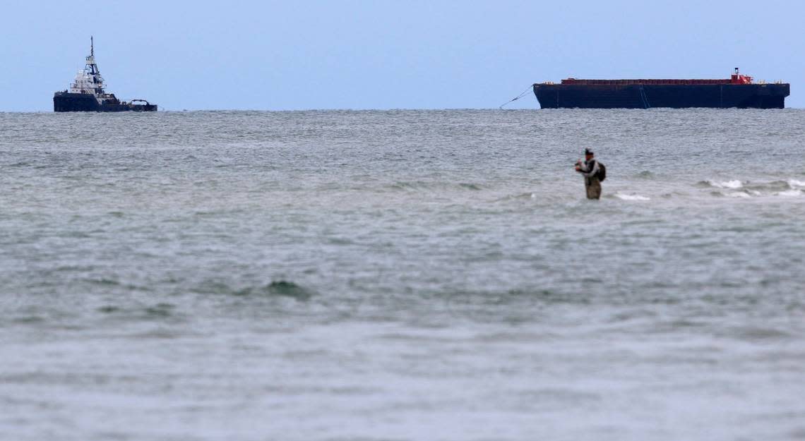 A fisherman casts out in the channel at Fort Macon at Morehead City on in June 2015. In the background a tug boat pulls a barge back after it took a load of sand out to sea that was dredged from the channel at the port in Morehead City.