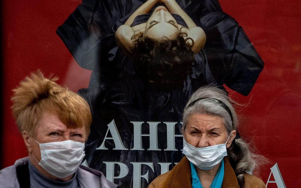Two women wearing face masks to protect against the coronavirus stand at a bus stop in Moscow - YURI KADOBNOV / AFP