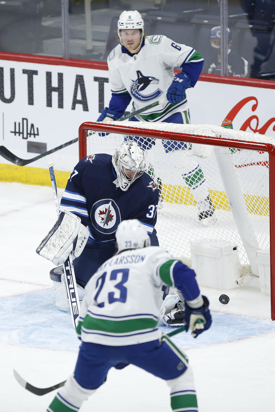 Vancouver Canucks' Brock Boeser (6) and Oliver Ekman-Larsson (23) watch as J.T. Miller's (9) shot gets past Winnipeg Jets goaltender Connor Hellebuyck (37) during the first period of an NHL hockey game, Thursday, Jan. 27, 2022 in Winnipeg, Manitoba. (John Woods/The Canadian Press via AP)