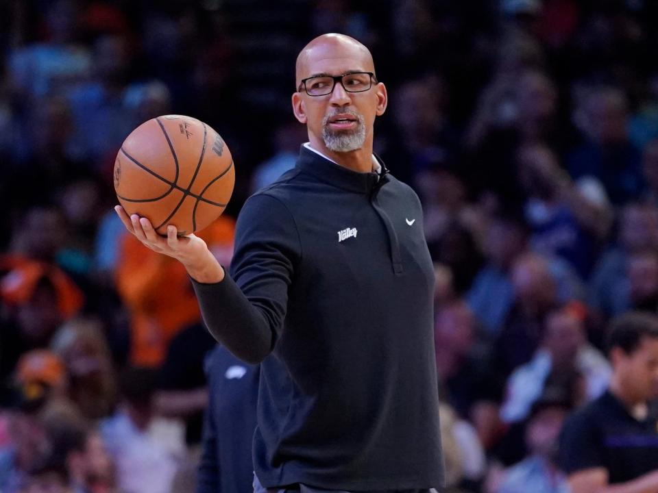 Monty Williams picks up a basketball and holds it out in his hand during a Suns game.