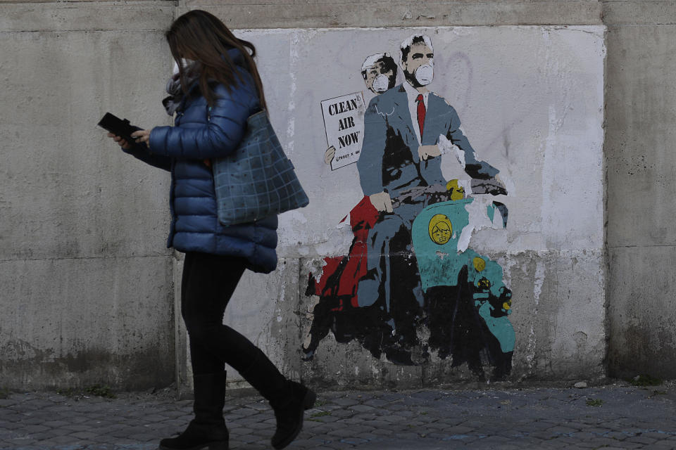A woman walks past a poster depicting a scene from the famed movie " Roman Holiday" with Gregory Peck and Audrey Hepburn wearing surgical masks as riding a Lambretta scooter in Rome, Friday, April 9, 2021. Italy has seen a stabilizing of the new variant-fueled infections over the past three weeks, though its daily death count remains stubbornly high, averaging between 300-500 COVID-19 victims per day, and its ICU capacity for virus patients is well over the threshold set by the government. (AP Photo/Gregorio Borgia)