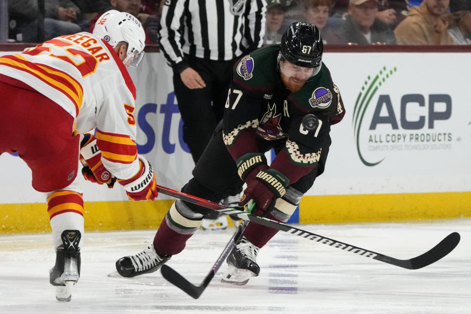 Arizona Coyotes left wing Lawson Crouse (67) loses the puck in front of Calgary Flames defenseman MacKenzie Weegar, left, during the third period of an NHL hockey game Thursday, Jan. 11, 2024, in Tempe, Ariz. (AP Photo/Ross D. Franklin)