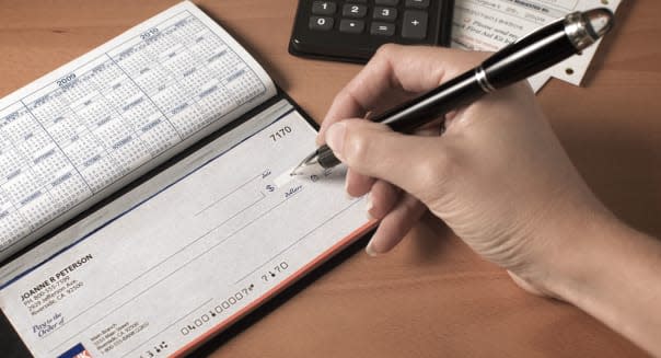 Writing a check to pay the bills with calculator and pen on desktop
