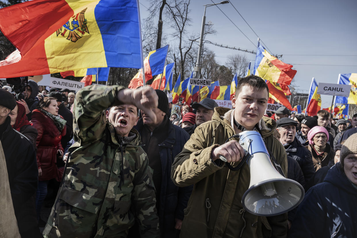 Protesters with Moldovan flags, one holding a bullhorn, gather in the streets.
