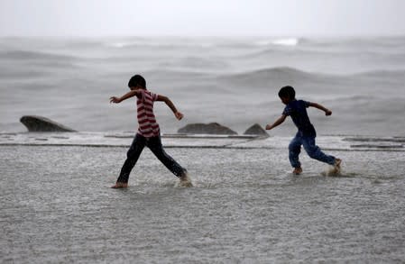 Children play in a puddle of water as it rains at a sea front in Kochi
