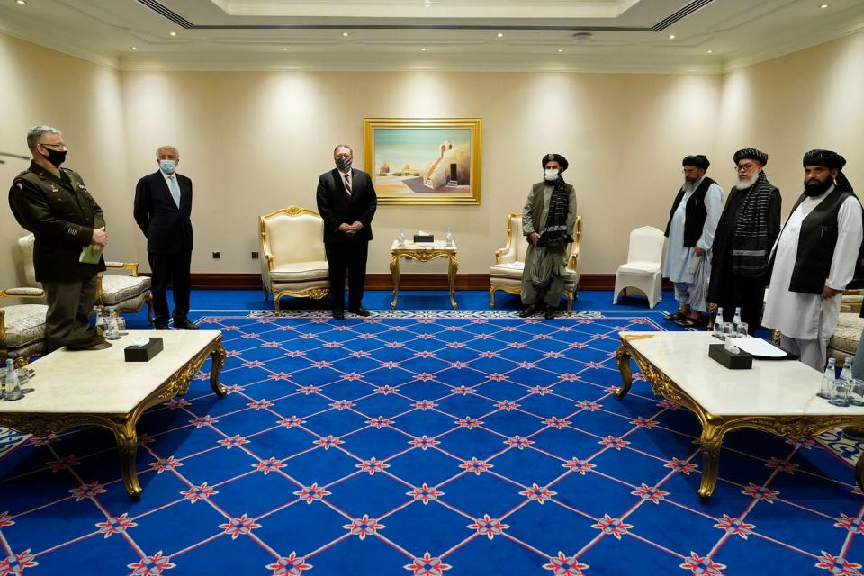 Men, some in suits and other in traditional Pashtun clothing, stand in a hotel conference room at a distance from each other, wearing face masks