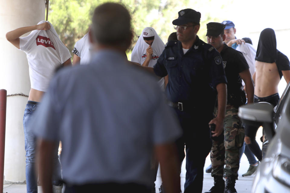 Suspects cover their faces with their shirts as they arrive at the Famagusta courthouse in Paralamni, Cyprus, Friday, July 26, 2019. A Cyprus court has ordered seven Israelis who were vacationing on the east Mediterranean island nation to be detained after a 19-year-old British woman alleged that she was raped in the resort town of Ayia Napa. (AP Photo/Petros Karadjias)