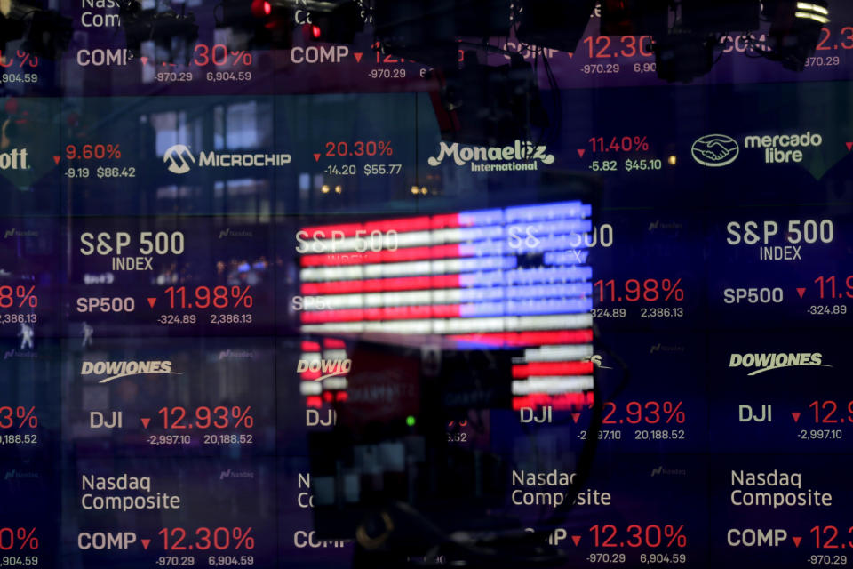 FILE - In this March 16, 2020, file photo, United States flag is reflected in the window of the Nasdaq studio, which displays indices and stocks down, in Times Square, New York. (AP Photo/Seth Wenig, File)