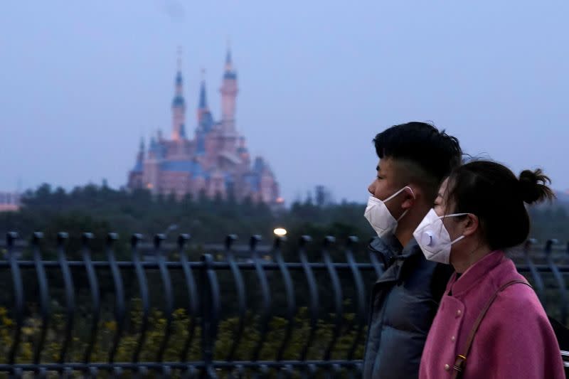 FILE PHOTO: Visitors wearing masks walk past Shanghai Disney Resort, that will be closed during the Chinese Lunar New Year holiday following the outbreak of a new coronavirus, in Shanghai