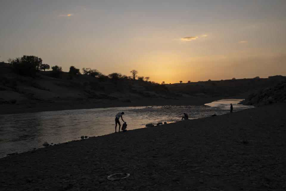 People stand on the banks of the Tekeze River, on the Sudan-Ethiopia border after Ethiopian forces blocked individuals from crossing into Sudan, near Hamdayet, eastern Sudan, on March 16, 2021. Ethiopia is at left, and Sudan is at right. (AP Photo/Nariman El-Mofty)