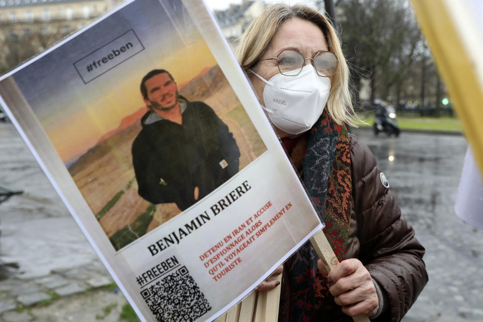 FILE - A woman holds a photo of Benjamin Briere during a rally in Paris, France, Saturday, Jan. 8, 2022. Two French citizens imprisoned in Iran have been freed, France's foreign minister said Friday. Benjamin Briere and Bernard Phelan, who both had been held in a prison in Mashad, in northwest Iran, were heading to Paris, a statement from Foreign Minister Catherine Colonna said. (AP Photo/Adrienne Surprenant, File)