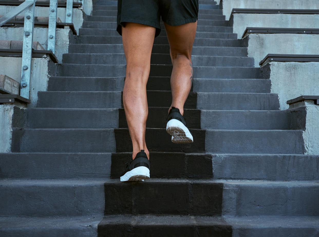 A man's legs, in shorts, climbing stairs, feet in athletic shoes, without his torso shown. 