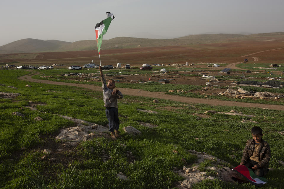 Bedouin boys play with Palestinian flags after Israeli troops demolished tents and other structures of the Khirbet Humsah hamlet in the Jordan Valley in the West Bank, Wednesday, Feb. 3, 2021. A battle of wills is underway in the occupied West Bank, where Israel has demolished the herding community of Khirbet Humsu three times in as many months, displacing dozens of Palestinians. Each time they have returned and tried to rebuild, saying they have nowhere else to go. (AP Photo/Maya Alleruzzo)